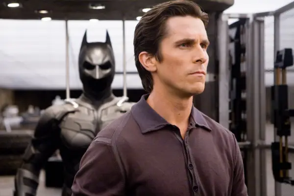 The Dark Knight - Medium shot of Christian Bale as Bruce Wayne with Batsuit in background.