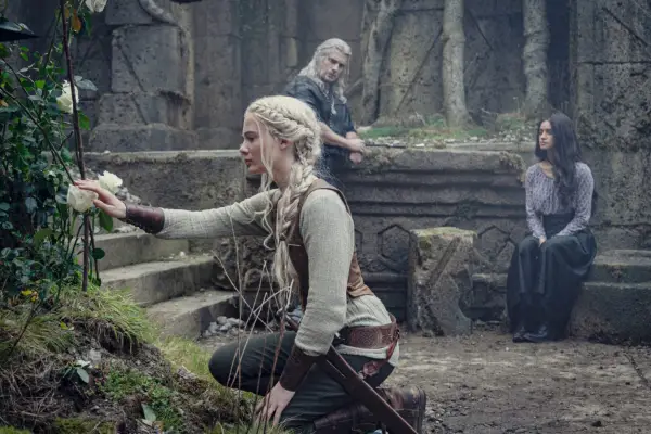 Ciri looking at a flower, with Geralt and Yennefer leaning in the background