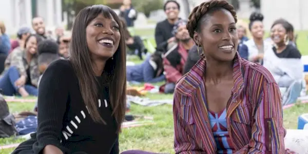 Yvonne Orji and Issa Rae as Molly and Issa sit on a blanket in a park and smile in Insecure.
