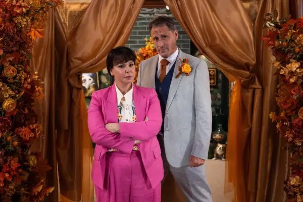 Nancy dressed in pink next to Tony in a grey suit in Hollyoaks