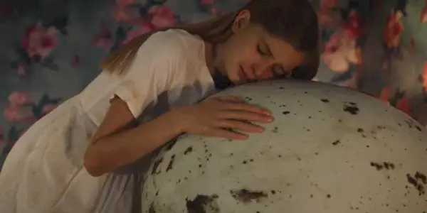 A young girl crying while presisng her cheek to a giant egg in Hatching