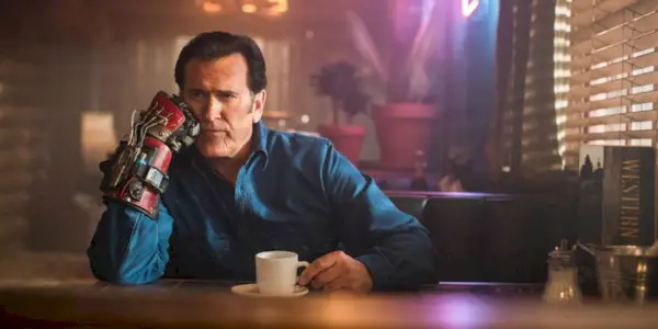 Ash, played by Bruce Campbell, sitting at the bar drinking coffee contemplatively in Ash vs Evil Dead