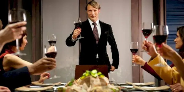 Mads Mikkelsen holding up a glass of wine with others in Hannibal