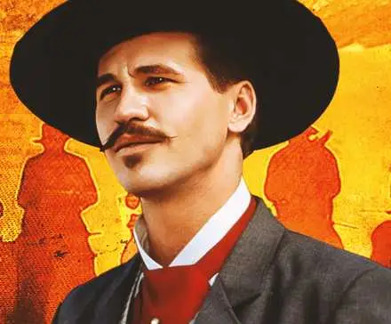 Actor Val Kilmer as Doc Holliday in Tombstone, smiling against an orange background of men on horseback.