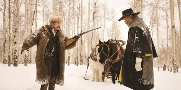 Kurt Russell as John Ruth aiming a rifle at Samuel L. Jackson as Maquis Warren in a snow covered forest in 