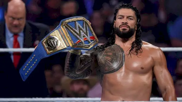 WWE star Roman Reigns holding up his championship belt in the ring.