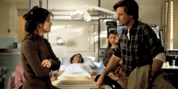 A woman and man talk in front of a man in a hospital bed in While You Were Sleeping.
