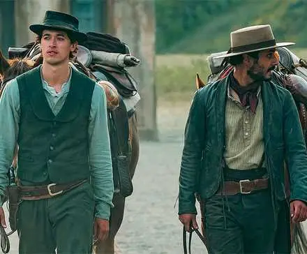 Tom Blyth as Billy the Kid walking with a horse next to another cowboy