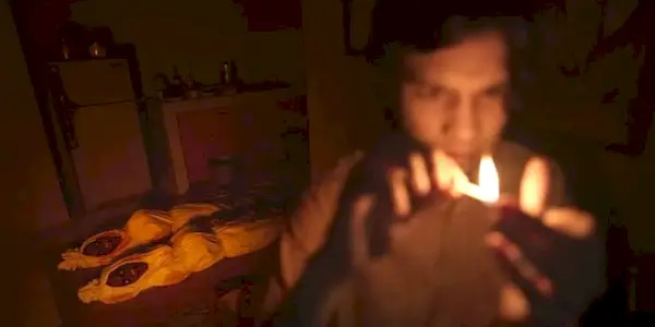 Two bodies look at a boy trying to light matches in a dark room in the Indonesian horror sequel Satan