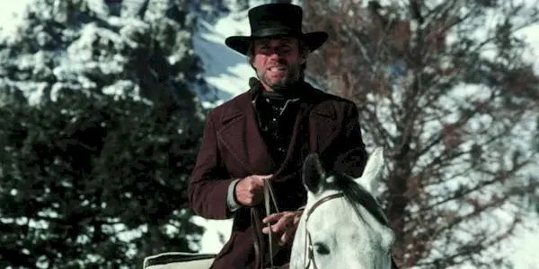 The Preacher (Clint Eastwood) rides through the snow on horseback in 