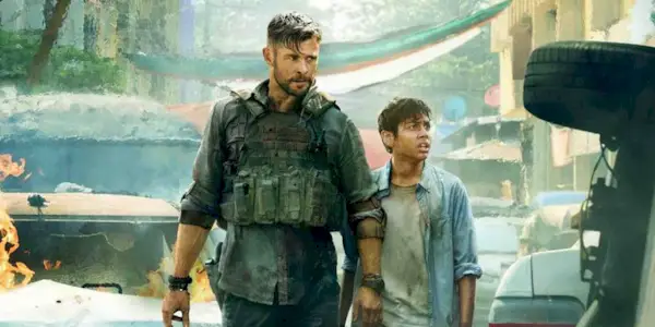 A man with military gear walking with a child on a street that is on fire