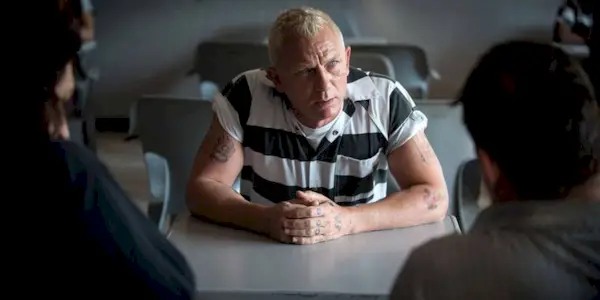 Joe Bang in a prison uniform talking to two visitors in Logan Lucky