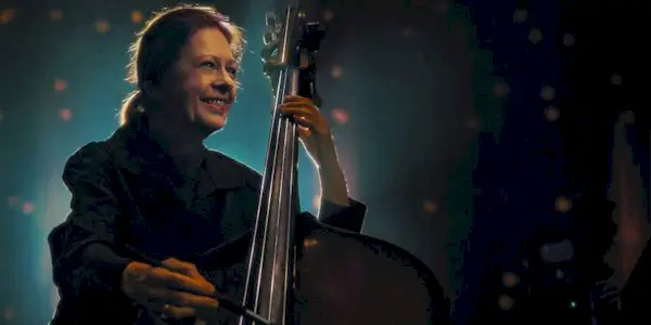 A woman smiling while playing the cello in The Only Girl in the Orchestra