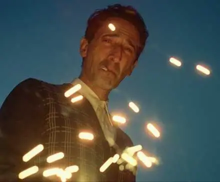 Adrien Brody staring at the ground with sparks rising in 