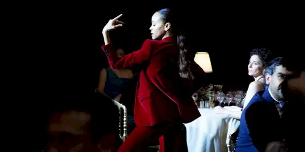 Zoë Saldaña dances in a red suit in a dark room around tables of people in Jacques Audiard
