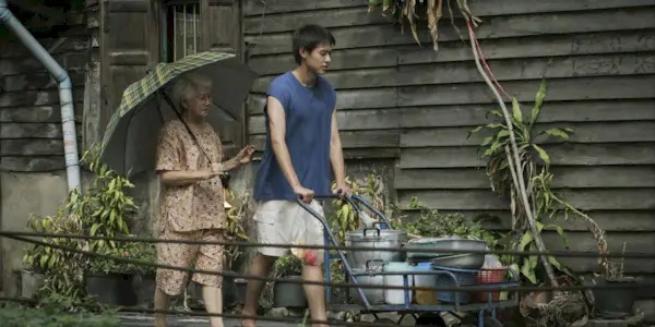 A boy pushes a cart walking next to his grandma (Usha Seamkhum) in How to Make Millions Before Grandma Dies