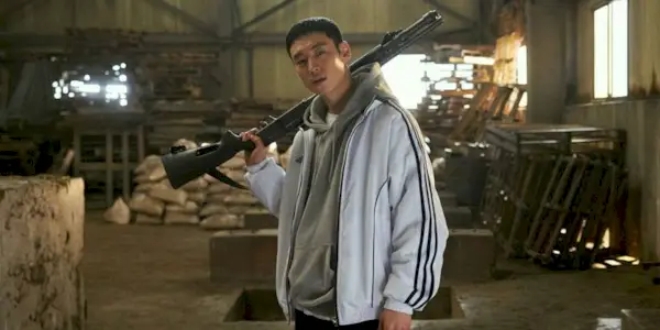 Lee Je Hoon holds a long gun over his shoulder in a warehouse in Time to Hunt.