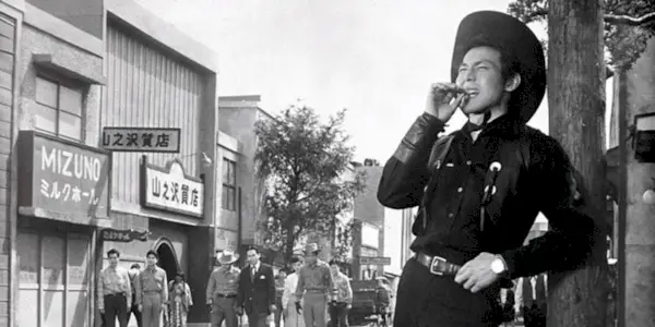 Joe Shishido as Joe the Ace leaning on a pole and grinning with a cigar in his mouth in Quick Draw Joe