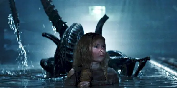Newt holding a baby doll whilst an alien stands behind her in 