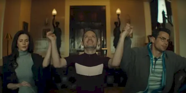 Elijah Wood and Theo James holding hands with a woman in The Monkey.