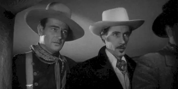 John Wayne and John Carradine standing next to each other looking at someone in Stagecoach