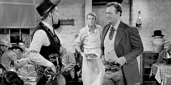 Lee Marvin and John Wayne talking while Jimmy Stewart stands behind them in The Man Who Shot Liberty Valance