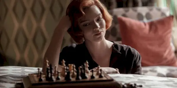 Anya Taylor-Joy as Beth Harmon sitting on a bed playing chess in The Queen