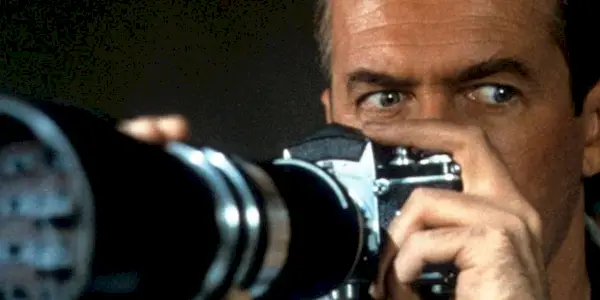 A photographer peers over his camera, intrigued yet concerned, as he aims his large lens out the window.