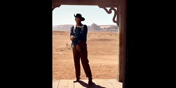 John Wayne as Ethan Edwards standing outside of a doorway in The Searchers