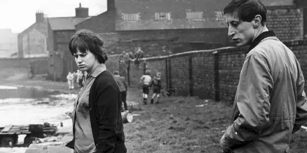 two people standing behind houses and a fence in Tony Richardson