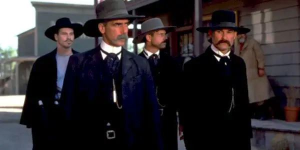 Sam Elliott, Kurt Russell, Val Kilmer, and Bill Paxton standing next to each other with Val Kilmer and Bill Paxton behind them in Tombstone