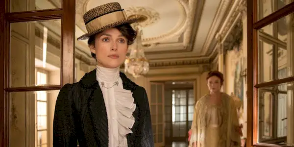 Colette looking ahead while a woman stands behind her in Colette.