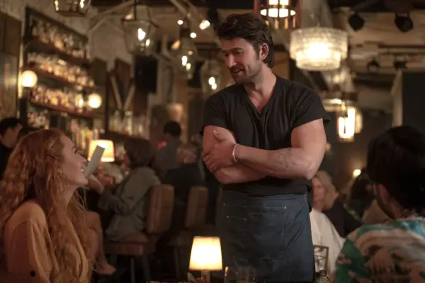 Blake Lively and Brandon Sklenar star in It Ends With Us chatting, with Lively sitting and Sklenar standing