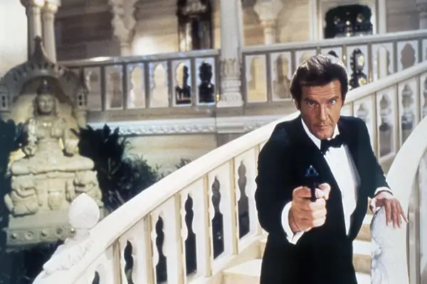 Roger Moore as James Bond in Octopussy standing on a bridge, wearing a tuxedo, holding a gun