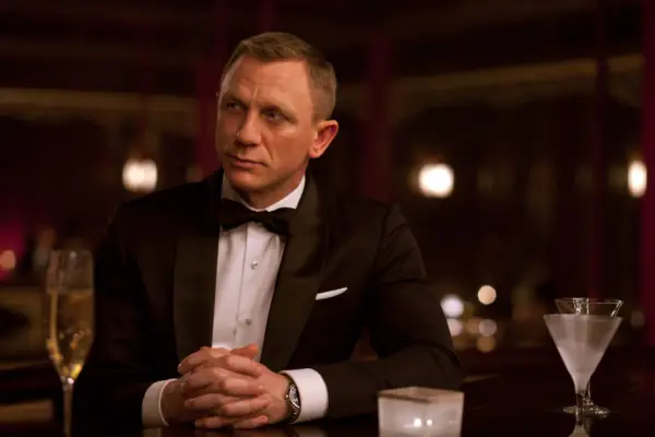 Daniel Craig as James Bond, sitting with his hands clasped, wearing a tuxedo