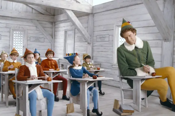 Will Ferrell in Elf, sat alongside a lot of smaller elf children in a classroom