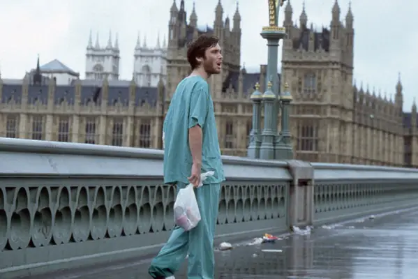 Cillian Murphy in 28 Days Later stood in scrubs holding a bag
