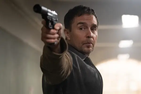Sam Rockwell as Aidan in Argylle. He is pointing a gun and looking serious