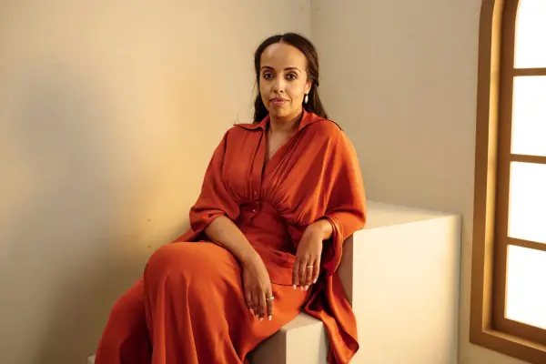 Nadia Latif wearing an rusty orange jumpsuit, sitting on a box.