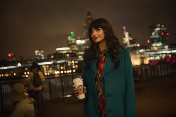 Jameela Jamil as Narrator in Love at First Sight wearing a blue coat, holding a Starbucks cup