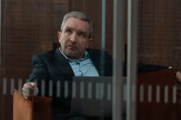 Eddie Marsan as Campbell in Fair Play, wearing a suit and blue shirt and sitting on a chair