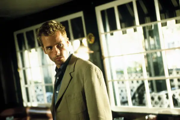 Guy Pearce as Leonard Shelby wearing a suit and looking over his shoulder in Memento.