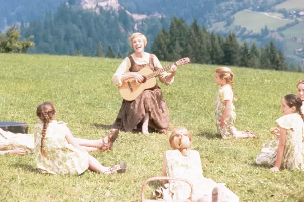 A woman and children gathered in a field in the mountains, singing