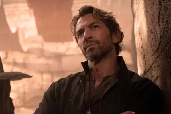 Gunnar stands with arms folded, looking inquisitively at something in the distance