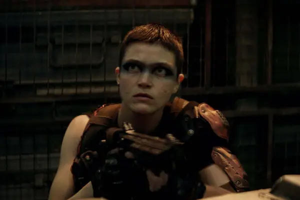 E Duffy plays Millius in Rebel Moon wearing brown armour, holding a gun