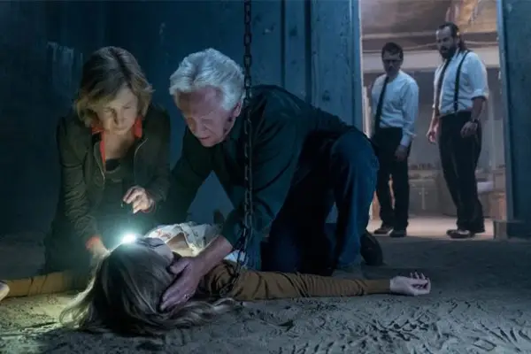 Two characters looking at a dead body, as two other characters look on