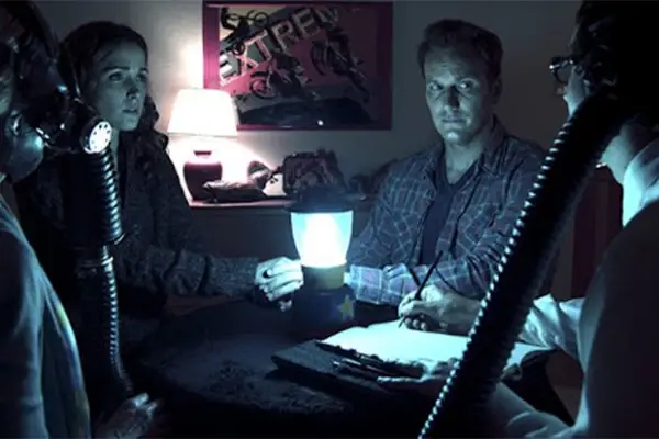 The characters of Insidious sat around a table with a lamp on it