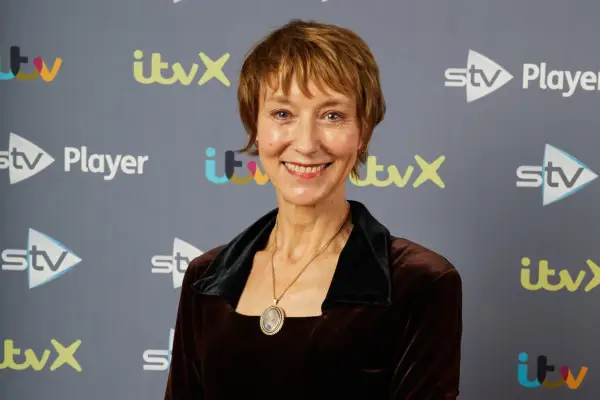 Connor Swindells as Jae Donnelly in Scoop, standing in a park and holding a camera.