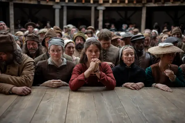 Jessie Buckley in Hamnet, leaning on the stage of the Globe theatre and clasping her hands together.