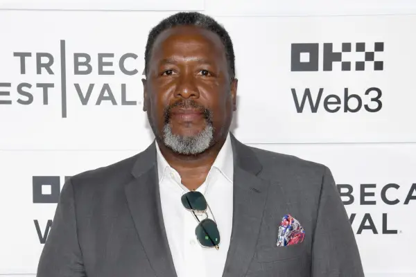 Wendell Pierce photographed at a film festival, wearing a grey jacket and white shirt, with his sunglasses hanging off the top button